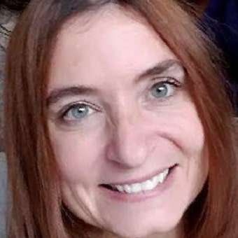 A woman with long brown hair smiles warmly at the camera, exuding the warmth and understanding often found in group counseling sessions.