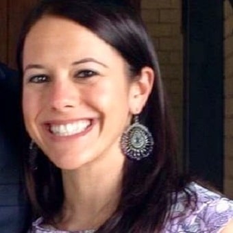 A woman with long dark hair smiles broadly, wearing large ornate earrings and a patterned top—her radiant energy suggests the positive influence of psychotherapy in her life.