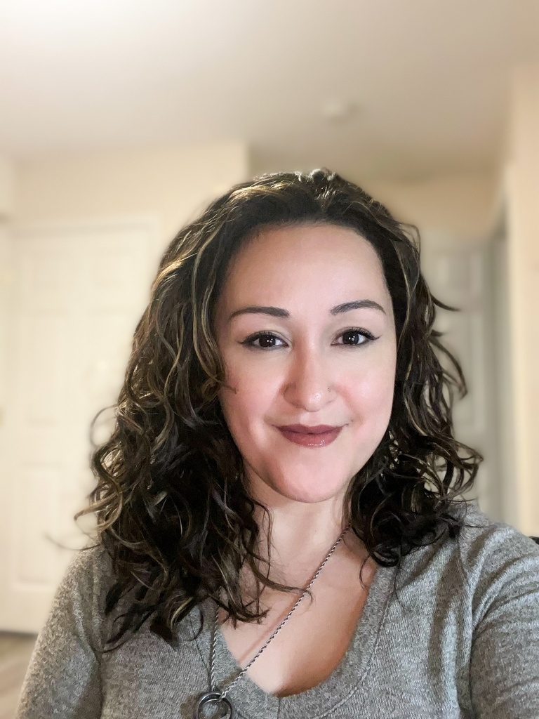 A person with curly hair and a neutral expression is standing indoors, perhaps waiting for an appointment at a mental health clinic.