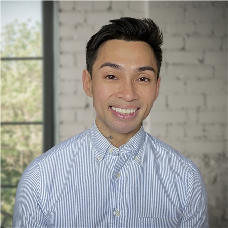 A person smiling, wearing a striped shirt, stands against a brick wall with a window in the background, embodying the warmth and positivity found at our best mental health clinic.