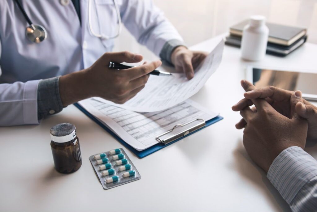 The best doctors ensure comprehensive care by discussing a medical report with patients at a desk, where a pill bottle and blister pack of capsules are visible, seamlessly integrating treatment approaches like psychotherapy for holistic healing.